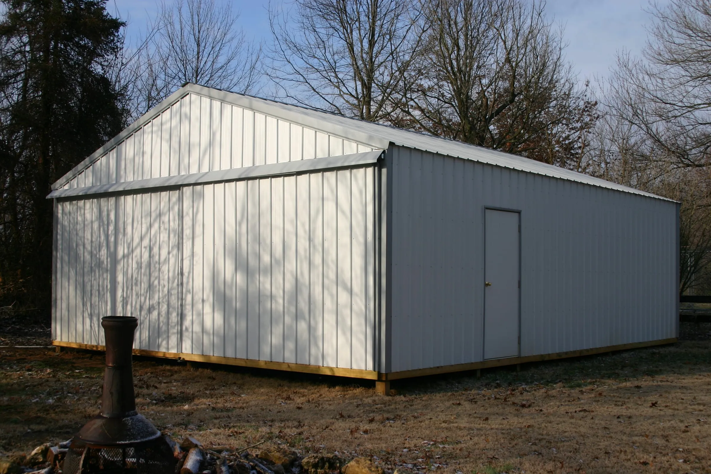 White building with gray gable trim and a walk door on a gravel pad