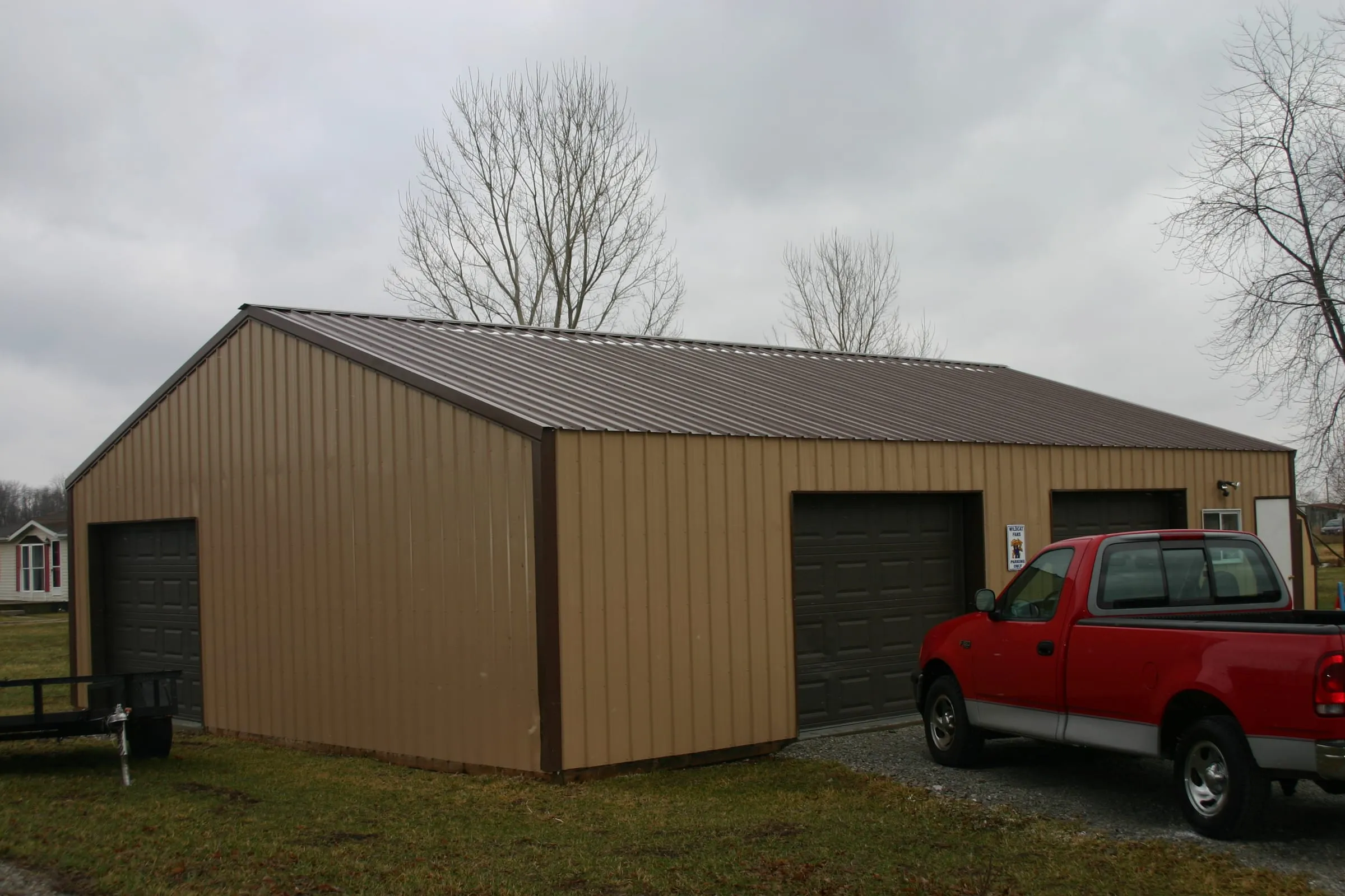 Tan building with a dark brown roof and two brown overhead doors, red pickup outside