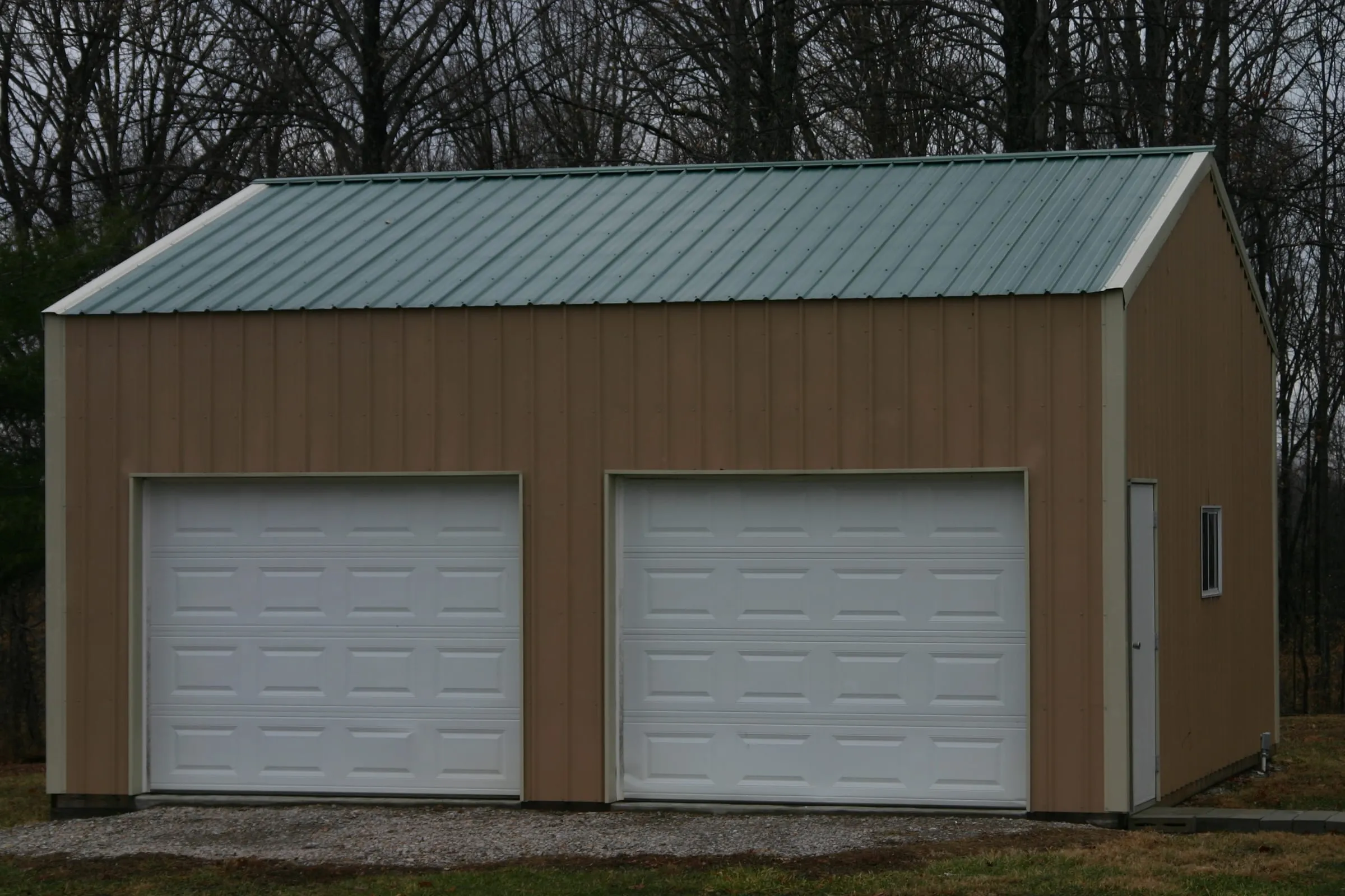Brown building with a green roof, two white overhead doors and a side window