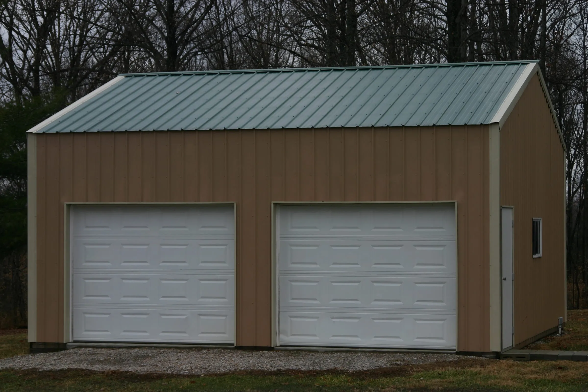 Brown building with a green roof and two white overhead doors, straight on