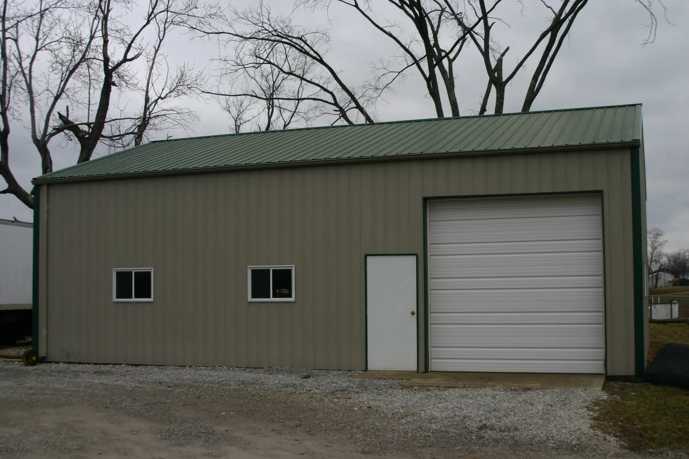 Olive green shop with white trim, two windows, a walk door and a white overhead door