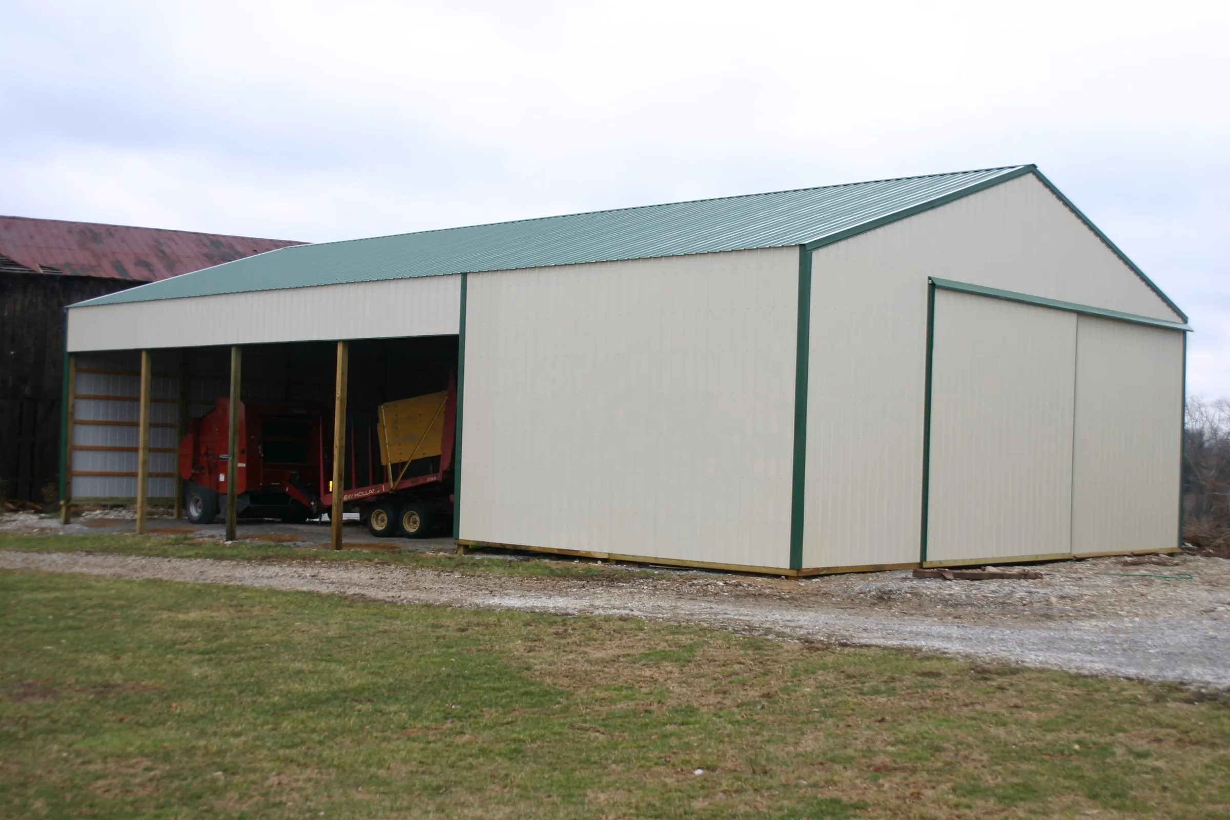Cream barn with green trim and an open lean-to with red equipment under it