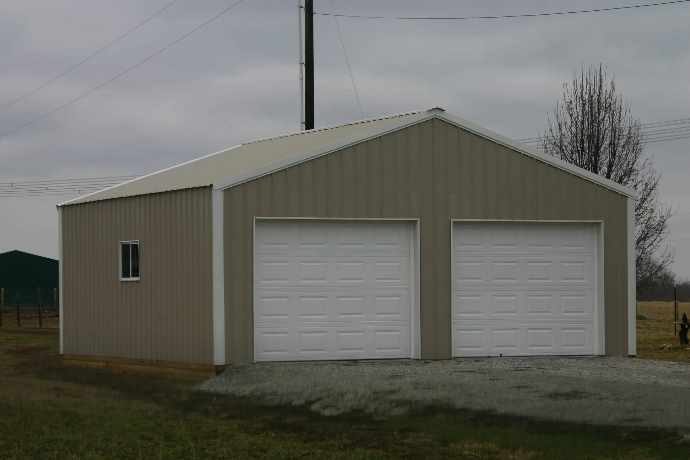 Tan building with brown trim, a window and two white overhead doors
