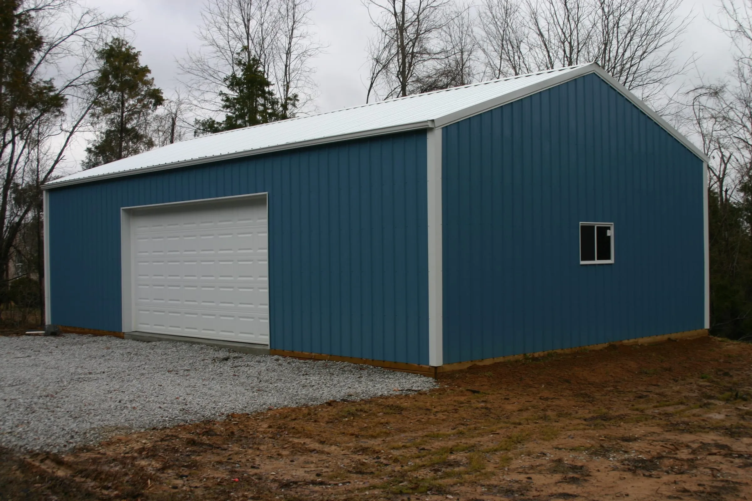 Blue building with white trim and a white overhead door on fresh gravel