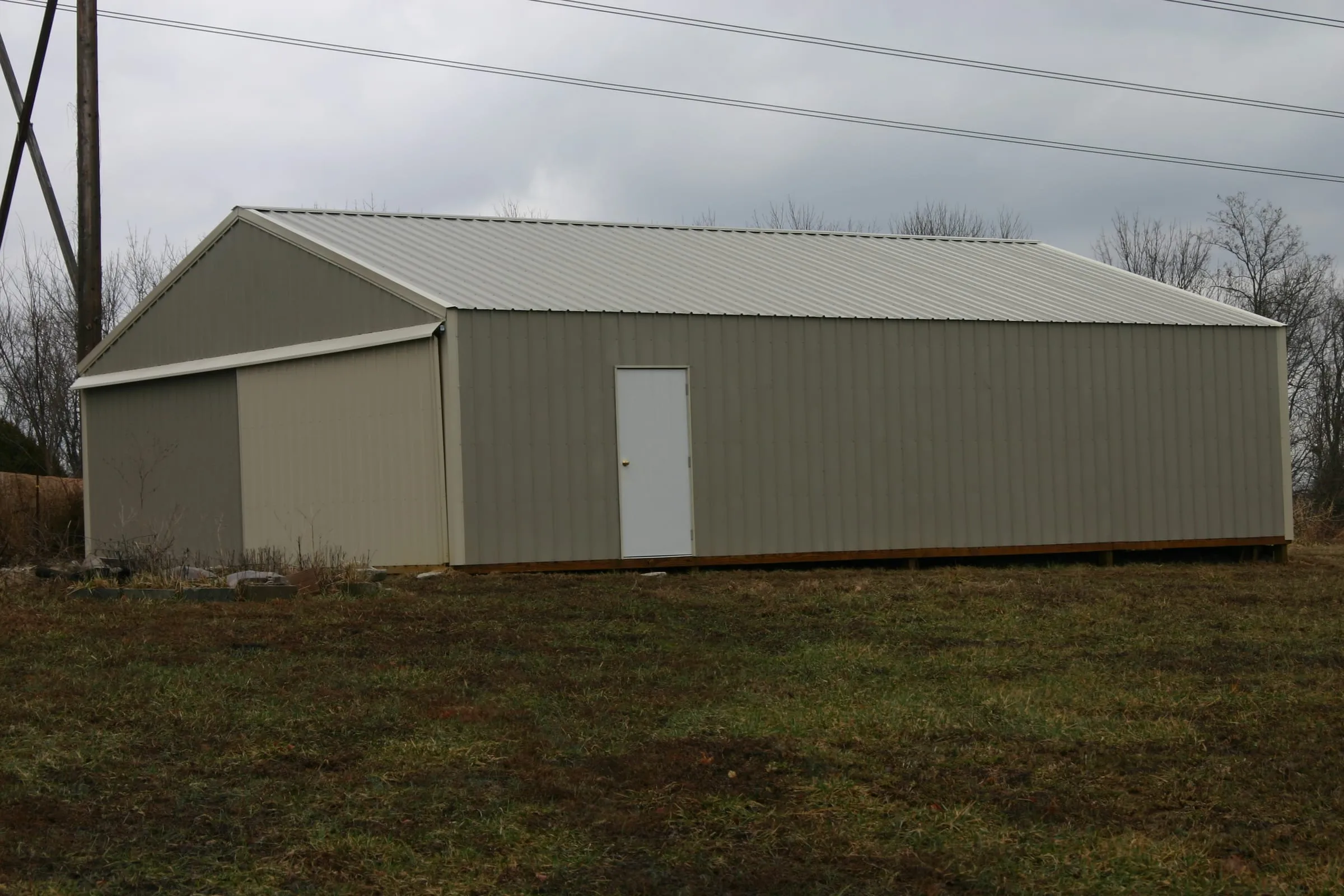 Tan building with a green roof and a walk door, seen from the gable end