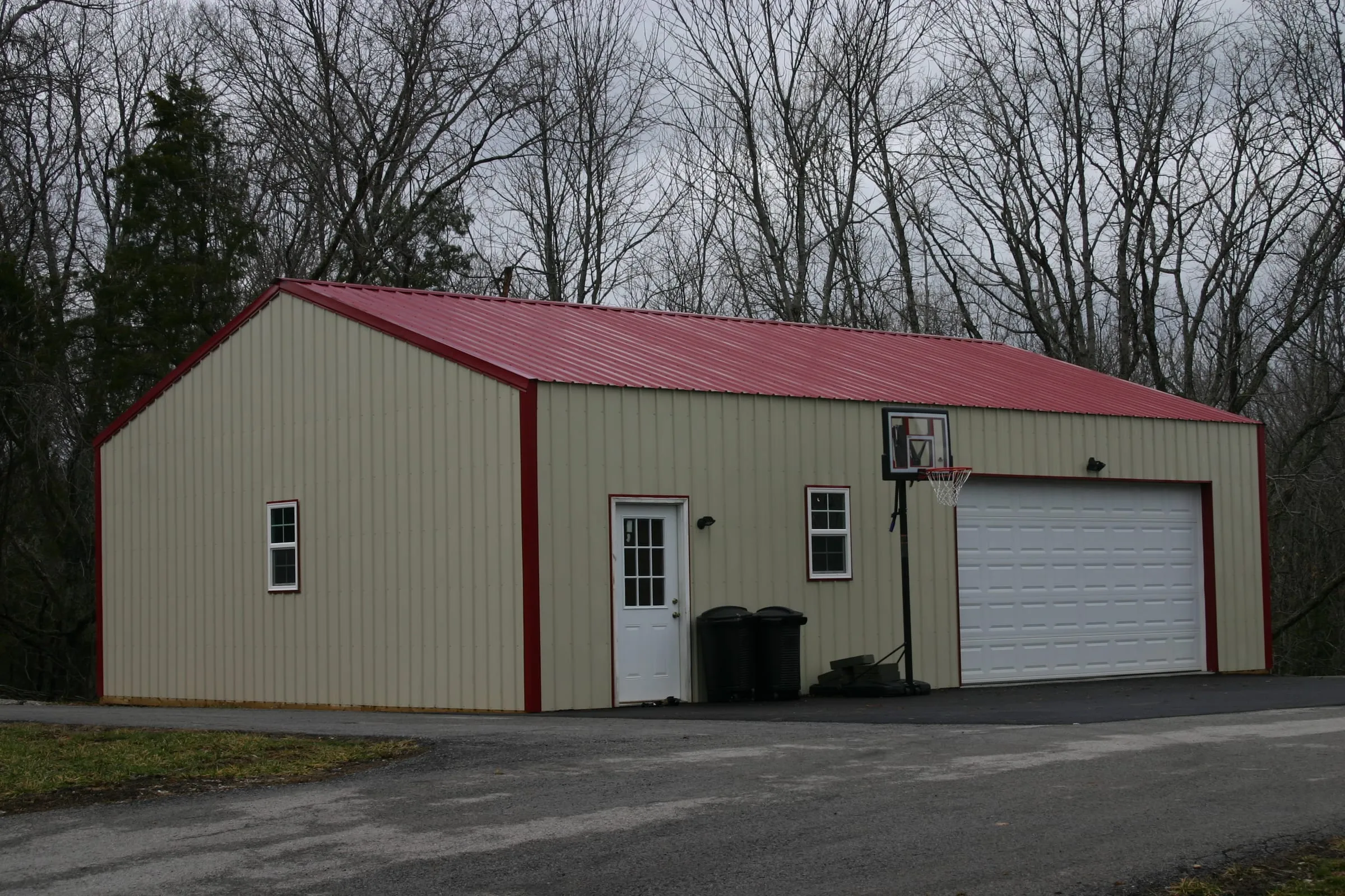 Cream shop with a red roof and red trim, a white overhead door, a walk door and two windows