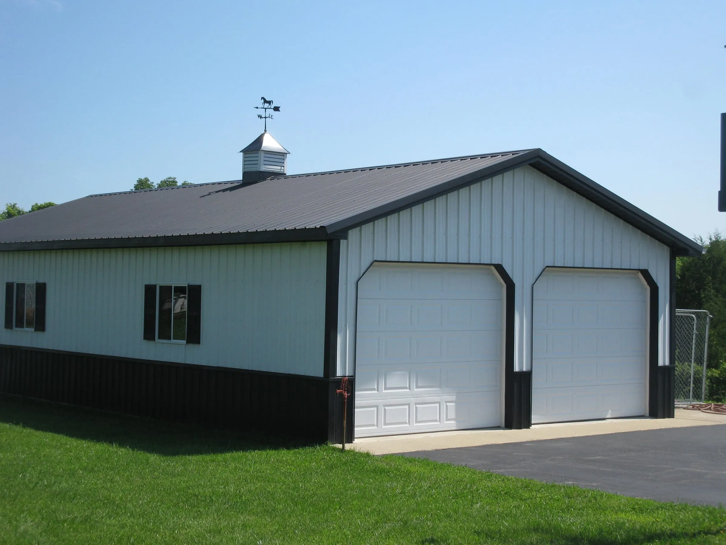 Pale blue shop with a dark roof and black wainscot, two white overhead doors and a cupola
